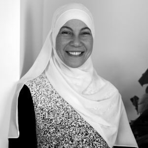 Facilitator Shaymaa Elkadi standing in front of a grey wall with a plant in the background